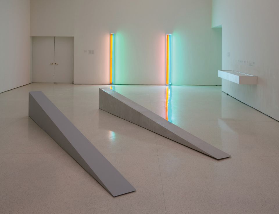 In foreground, two fabrications of Robert Morris's Untitled (Door Stop), 1965. (On left: 2018 artist-supervised, museum-made plywood fabrication; on right: 1965 fiberglass fabrication).  On far wall: two fabrications of Dan Flavin's Untitled (to Henri Matisse) 1964. (On left: historical fabrication received from Panza; right: 1995 fabrication produced in coordination with the Flavin studio)  